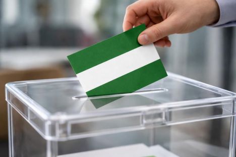 Una mano introduce una papeleta de la bandera de Andalucía en una urna electoral durante las elecciones.